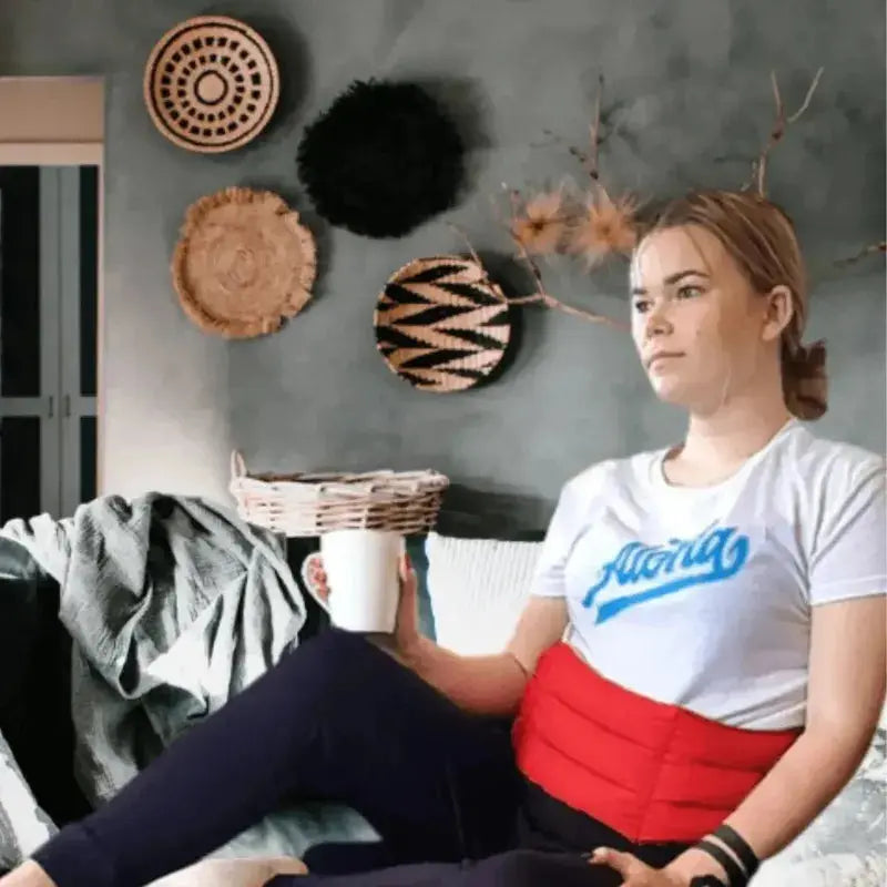 Lady sitting on the couch with a waist wheat bag round her tummy