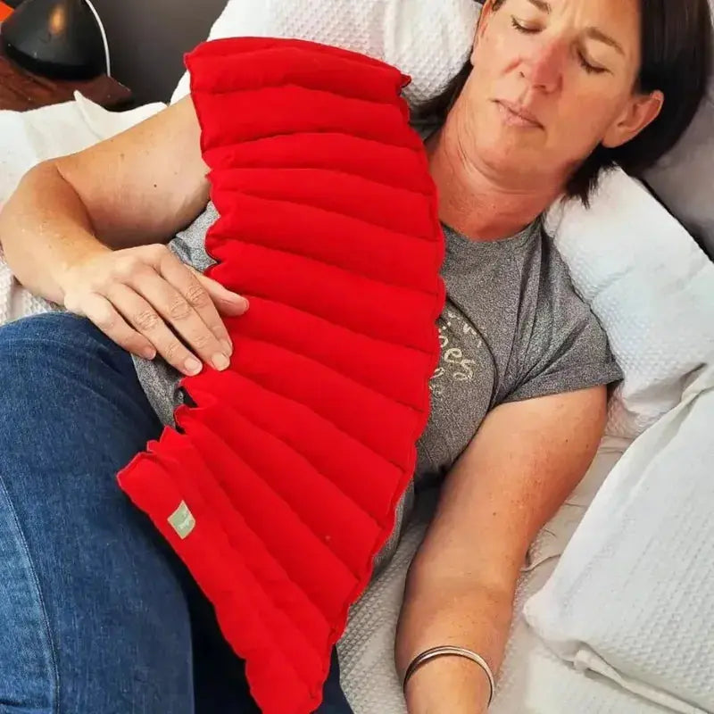 Lady laying on the bed with the neck wheat bag draped over her like a heated blacket